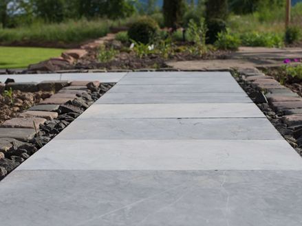 Blåstensfliser som havesti med blomsterbede og en grøn græsplæne i baggrunden