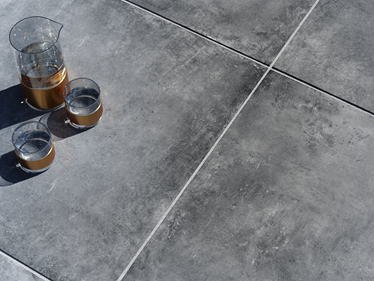 Mørk Vulkano-terrasseplade i betonlook med karaffel og glas