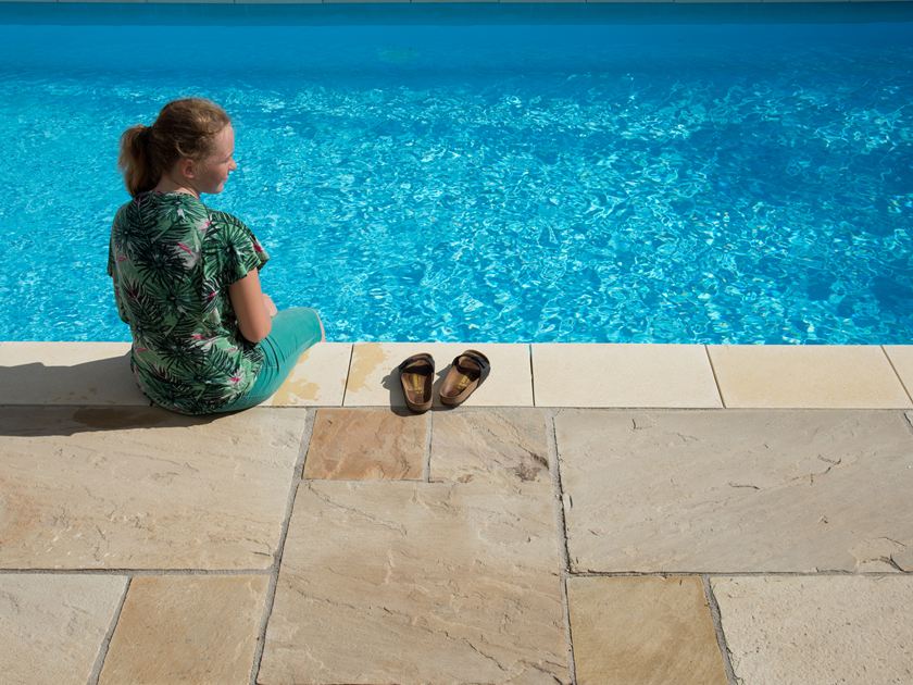 Pige sidder ved blå pool med sandstensplader Yellow Mint