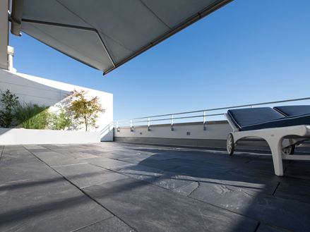 Tagterrasse med skifergulv og liggestole på kanten med udsigt i frøperspektiv