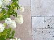 Beige travertinplader lagt i et romersk bånd med hvide blomster fra oven