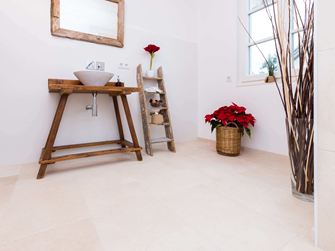 Badeværelse med træmøbler og lyse, naturlige kalkstensfliser som gulvbelægning