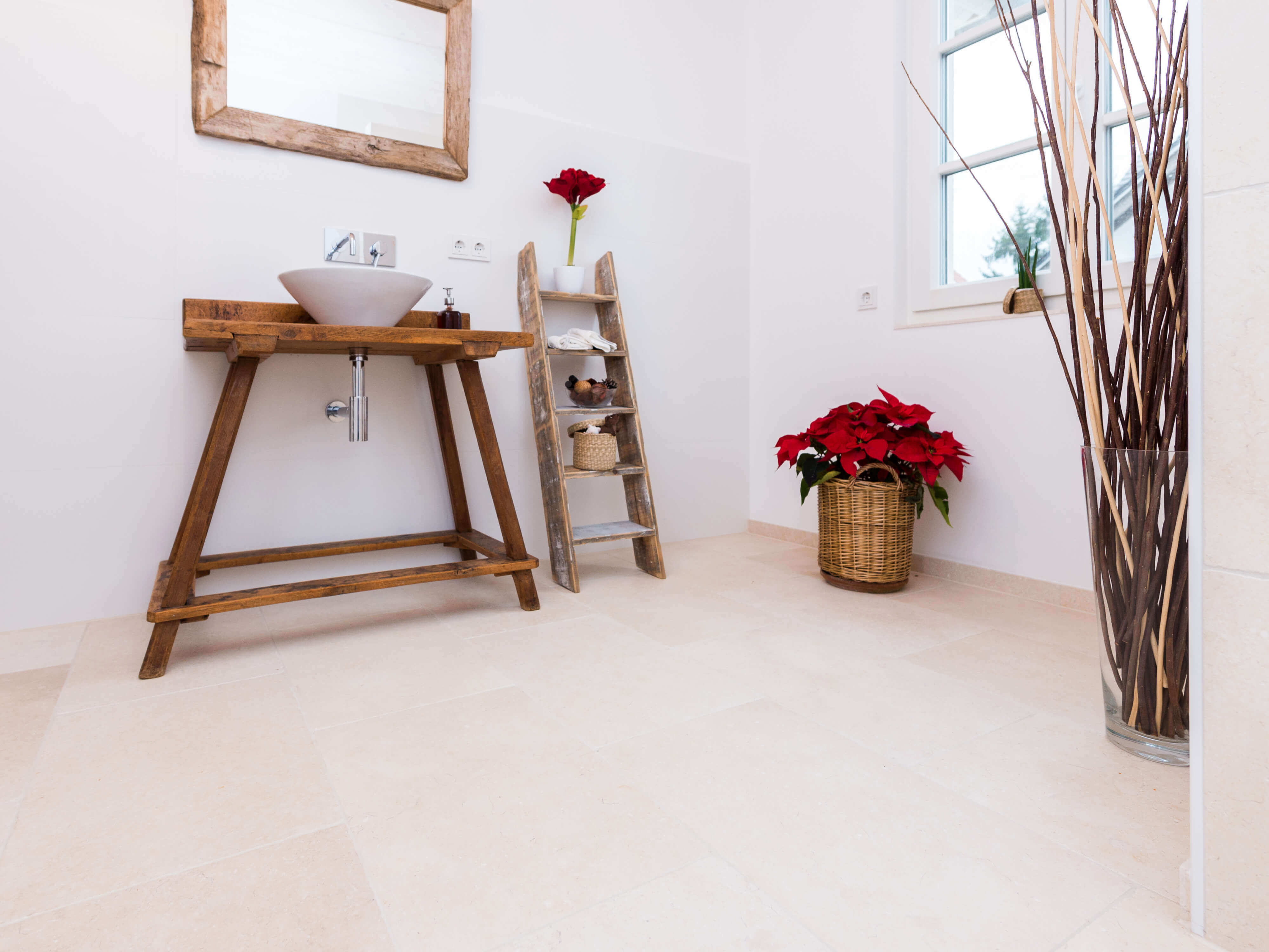 Badeværelse med træmøbler og lyse, naturlige kalkstensfliser som gulvbelægning