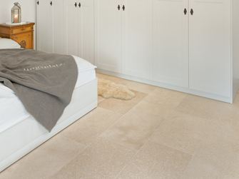 Soveværelse med hvidt klædeskab og hvid seng, beige kalkstensfliser på gulvet