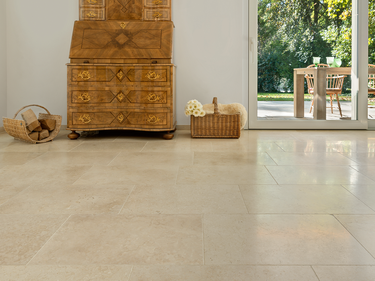 Harmoniske beige toner: Cleopatra Light kalkstensflise Antikt træskab på lyse kalkstensfliser Cleopatra Light, i baggrunden udsigt over terrassen og haven