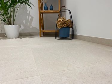 Nærbillede af gulv med Sevilla Cream Fliser i stentøj i et kalkstenslook. En træhylde, en plante og dekorationer i baggrunden.