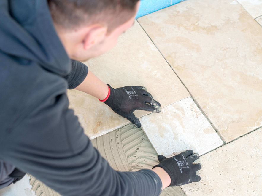 Mand lægger travertinfliser i lys beige i romersk bånd