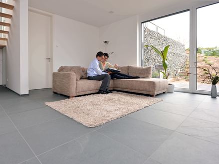 Storformat Grey Slate-skiferfliser i stuen med lys sofa og hvide vægge. Et par sidder i sofaen