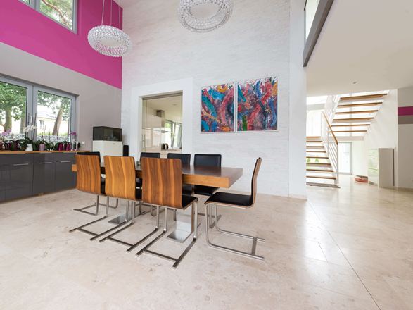 Åben spiseplads med moderne træstole og farverigt maleri på væggen, gulv i lyse travertinfliser med poleret overflade