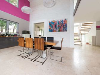 Åben spiseplads med moderne træstole og farverigt maleri på væggen, gulv i lyse travertinfliser med poleret overflade