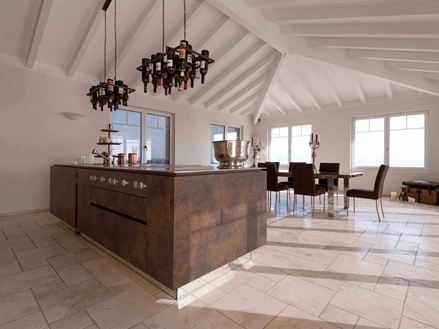 Køkkenø med vinflaskeholder i loftet, spisebord og stole i baggrunden på lagt travertin Light med tumlet, uglattet overflade