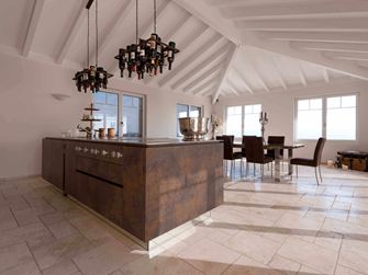 Køkkenø med vinflaskeholder i loftet, spisebord og stole i baggrunden på lagt travertin Light med tumlet, uglattet overflade