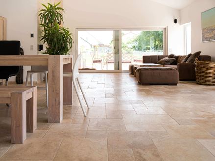 Stue med brun sofa, hvide vægge og medium travertinfliser i brun-beige som gulvbelægning