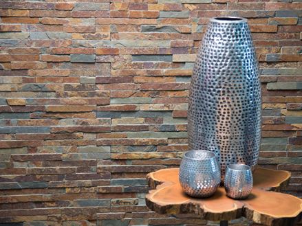 En stor og to små vaser i sølv foran farverige vægpaneler i skifer