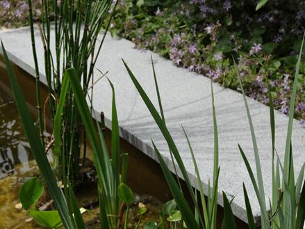 Universalplade som omkransning af en dam med græs i forgrunden