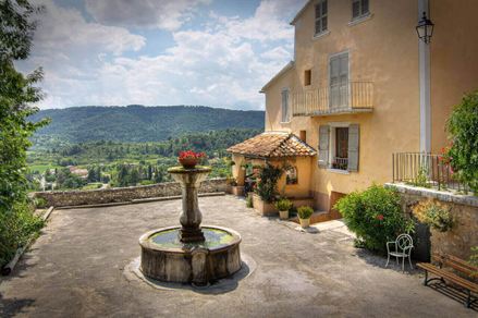 Et springvand på en plads ved siden af et landsted, bjerge i baggrunden