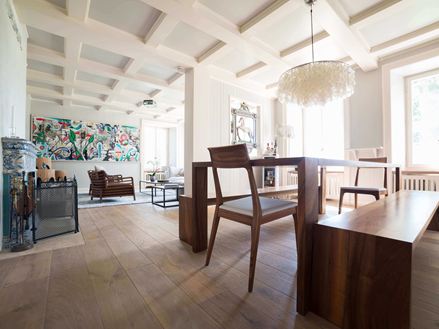 Moderne opholds- og spisestue med højt, hvidt loft, trægulv og et moderne maleri i baggrunden