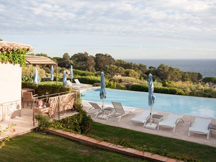 En pool med hvide liggestole og travertinplader med havet i baggrunden.