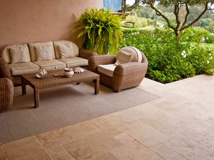 Indgangsparti på et middelhavshotel med kurvelænestole, travertingulv og en grøn have i baggrunden