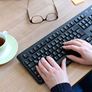 Hænder på tastaturet, briller og en kop kaffe ved siden af