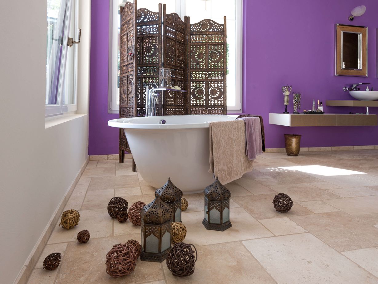 Fliserne Travertine Light i et badeværelse med fritstående badekar og lilla væg i baggrunden