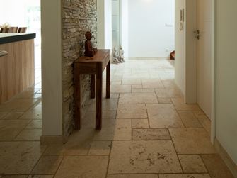 Gang med Light travertinfliser på gulvet, lille træbord og naturstenspaneler på den ene væg