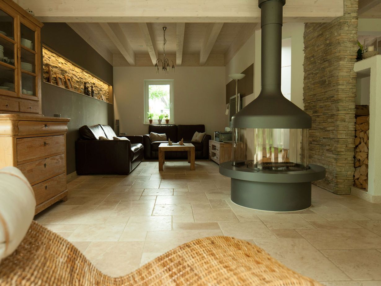 Stue med fritstående pejs og siddegruppe på Light travertinfliser, en kurvelænestol i forgrunden