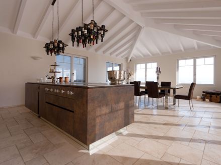 Køkkenø med vinflaskeholder i loftet, spisebord og stole i baggrunden på lagt travertin Light med tumlet, uglattet overflade