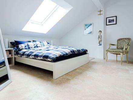 Et lyst soveværelse under taget med Medium Line travertinfliser som gulvbelægning