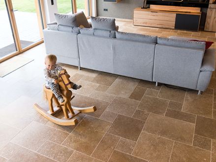 Barn sidder på en gyngehest og leger i stuen med Noce SELECT travertingulv