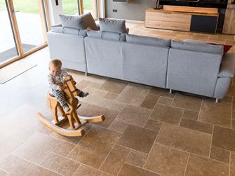 Barn sidder på en gyngehest og leger i stuen med Noce SELECT travertingulv
