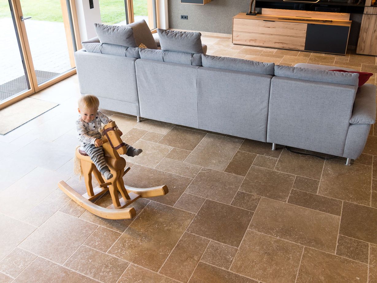 Barn sidder på en gyngehest og leger i stuen med Noce SELECT travertingulv