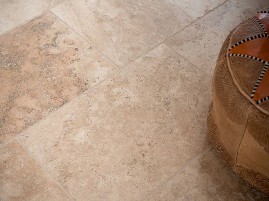 Rustikke travertinfliser lagt i brun og beige med dekorative puder
