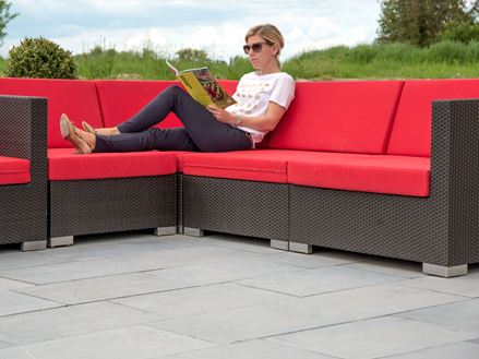 Kvinde sidder på moderne sofamøbler med røde puder på en blå terrasse