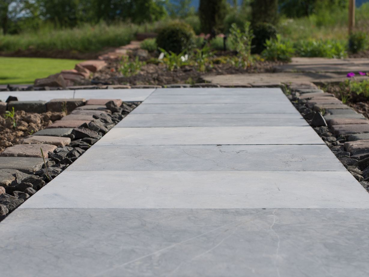 Blåstensfliser som havesti med blomsterbede og en grøn græsplæne i baggrunden