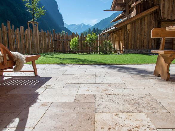 Terrassegulv med travertin rustic og træmøbler, i baggrunden en græsplæne og udsigt til bjergene