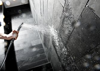 Hånd, der holder et brusehoved mod en væg med mørke stenfliser