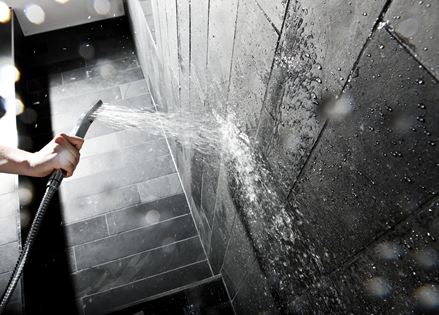 Hånd, der holder et brusehoved mod en væg med mørke stenfliser