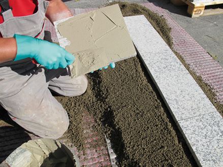Installatøren belægger bagsiden af stenen med klæbemiddel til lægning med enkeltkornsmørtel på ballastbasislag
