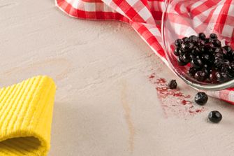 Gul klud, rødt viskestykke og en glasskål med bær væltet ud på natursten