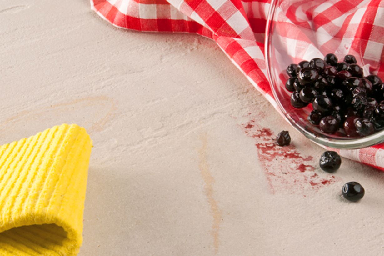 Gul klud, rødt viskestykke og en glasskål med bær væltet ud på natursten