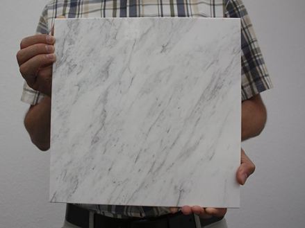 Person, der holder en hvid marmorflise med grå årer i kameraet