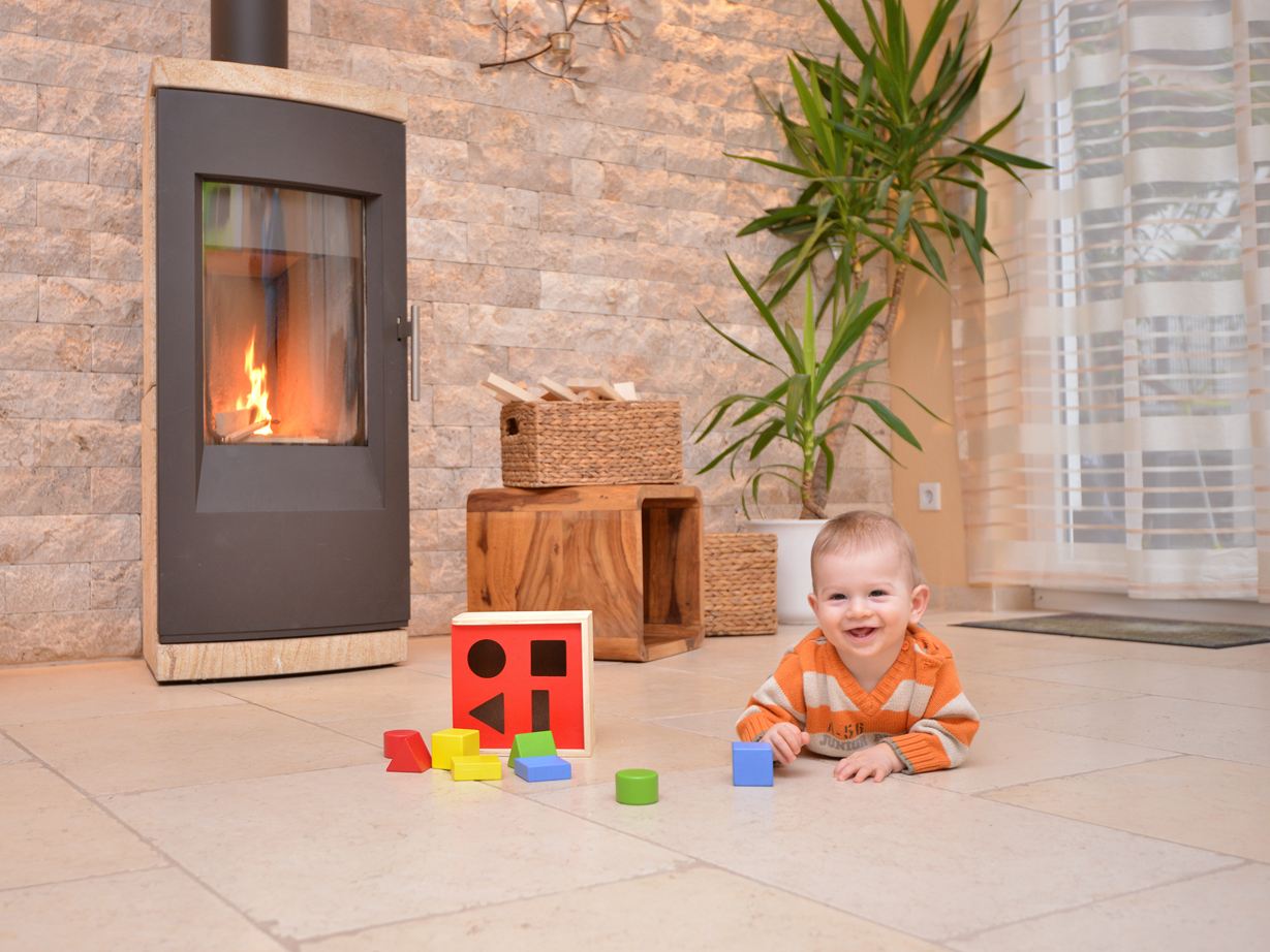 Baby leger på et naturstensgulv foran en pejs