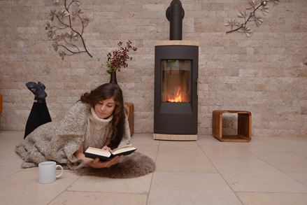 Kvinde ligger på kalkstensfliser foran en væg med naturstenspaneler og pejs og læser en bog