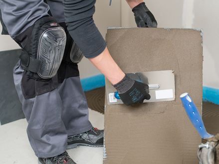 En flisemurer påfører klæbemiddel på bagsiden af en flise