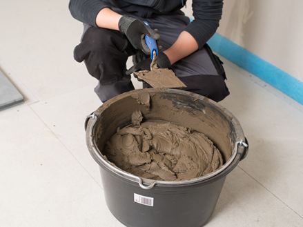 Flisemurer foran en spand med naturstensklæber