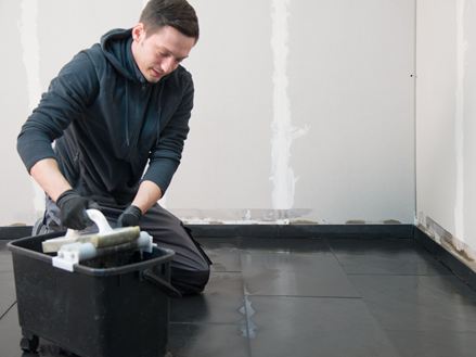 Flisemanden knæler på det udlagte skifergulv og vasker overskydende fuger af
