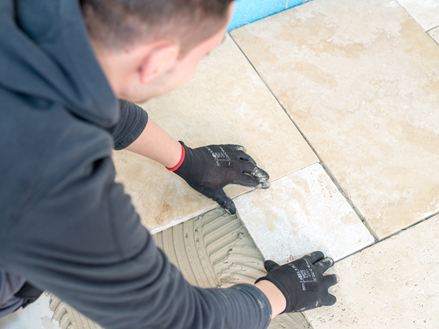 En flisemurer lægger en travertinflise i klæbebedet
